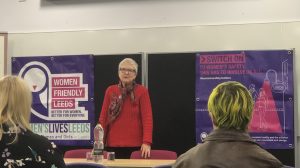 Photo of Councillor Garthwaite standing behind a desk. Speaking on Women's Safety to an audience with Women Friendly Leeds logo behind