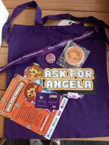 An image of goody bags from the event, including a purple tote bag, ask for angela flyers, and a biscuit from the biskery